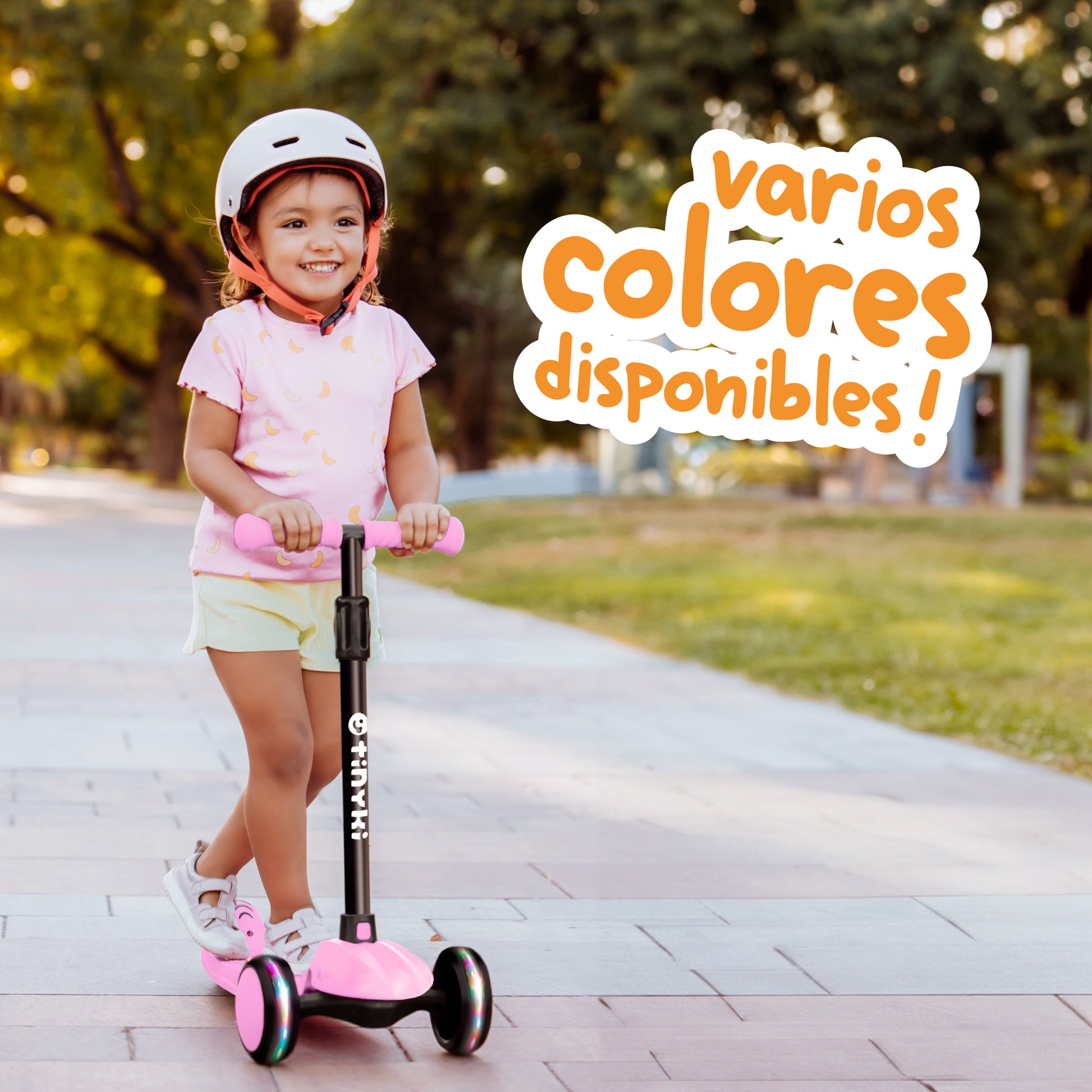 Niña disfrutando de su paseo en un patinete rosa Spidi de Tinyki, con texto destacando 'varios colores disponibles'. Patinete seguro y ajustable, perfecto para niños